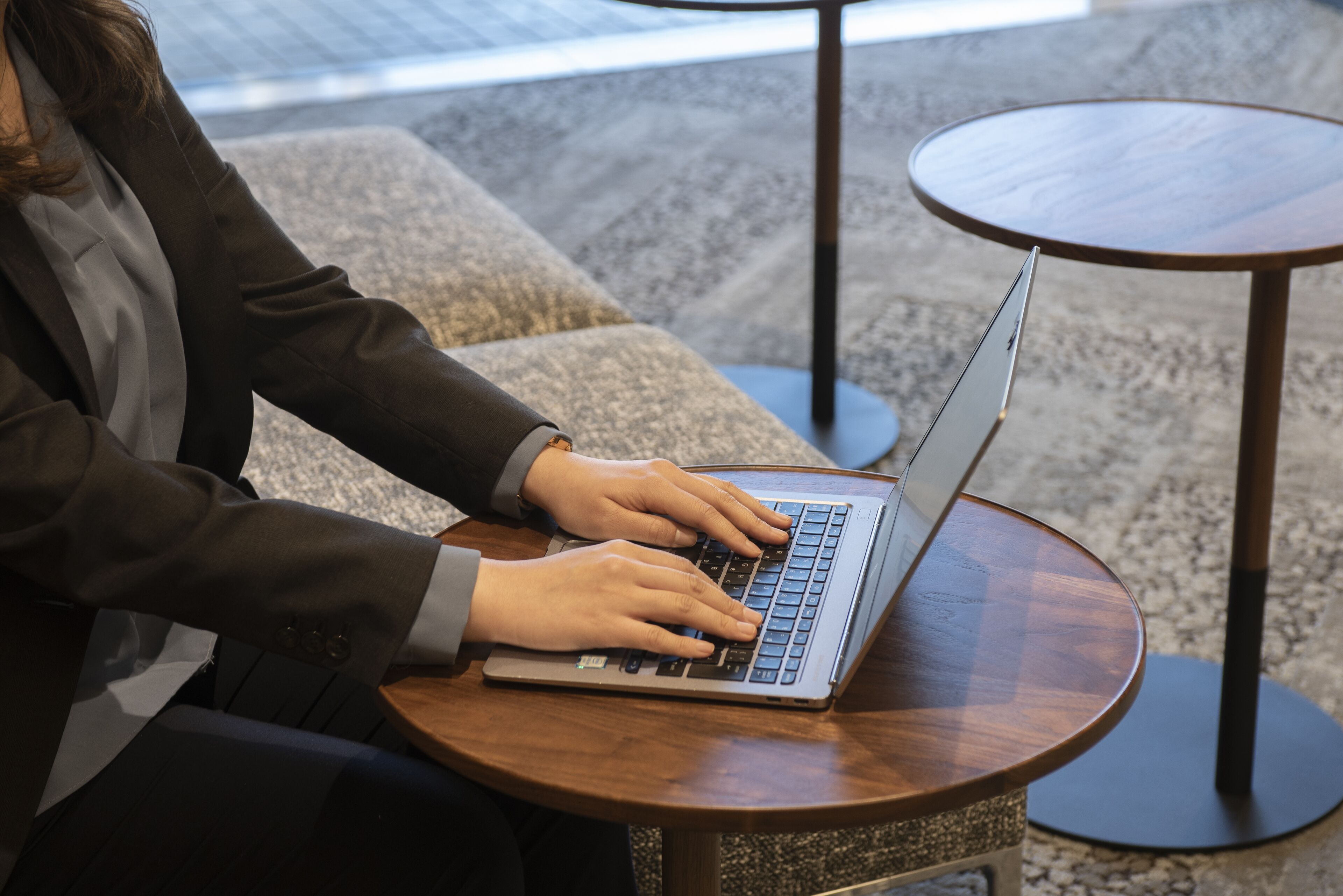 A person using a laptop on a round wooden table in a modern indoor setting.