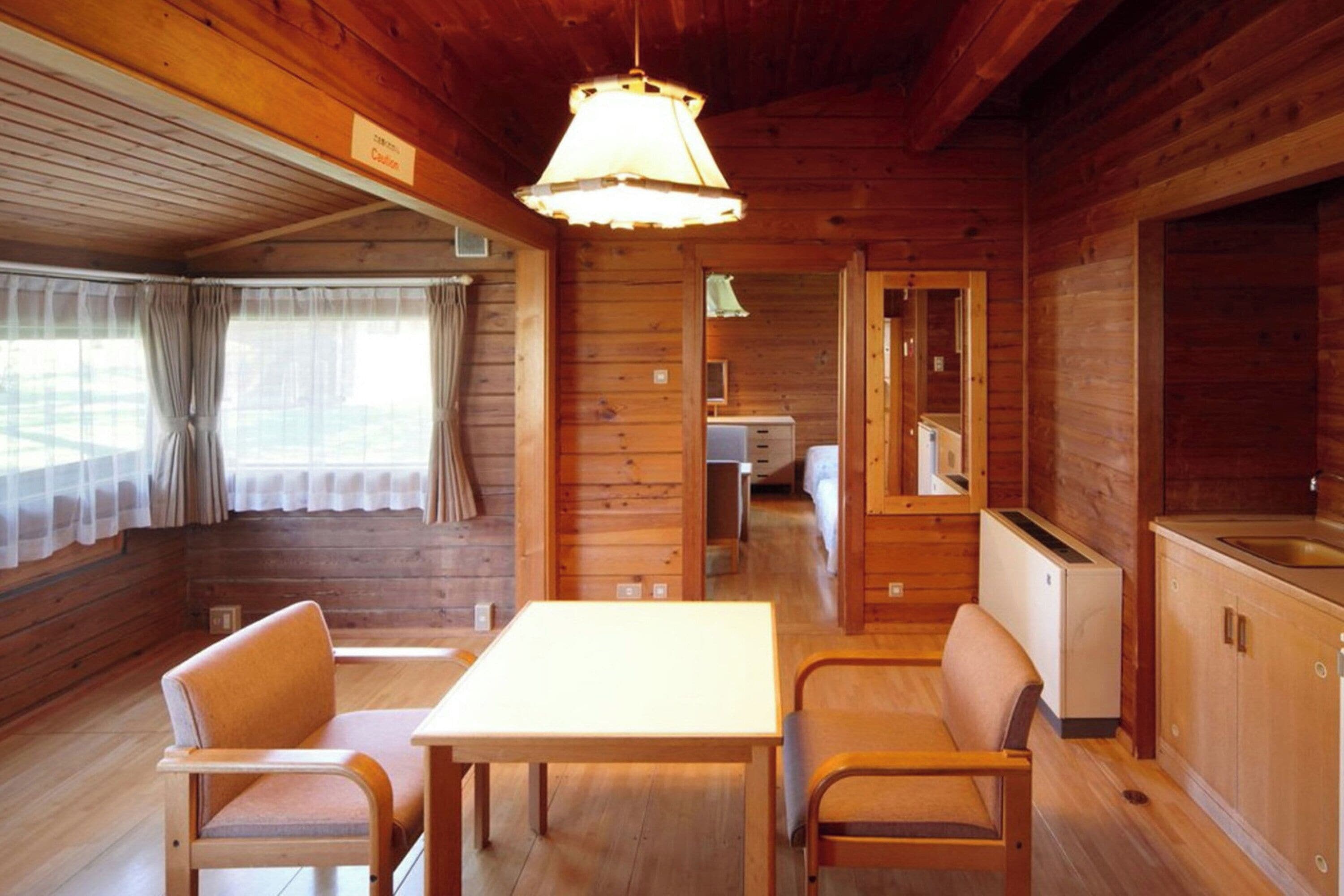 A wooden cabin interior with a dining table and chairs, a kitchenette, and a small bathroom.