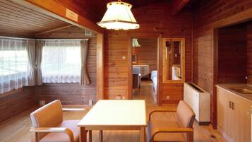 A wooden cabin interior with a dining table and chairs, a kitchenette, and a small bathroom.