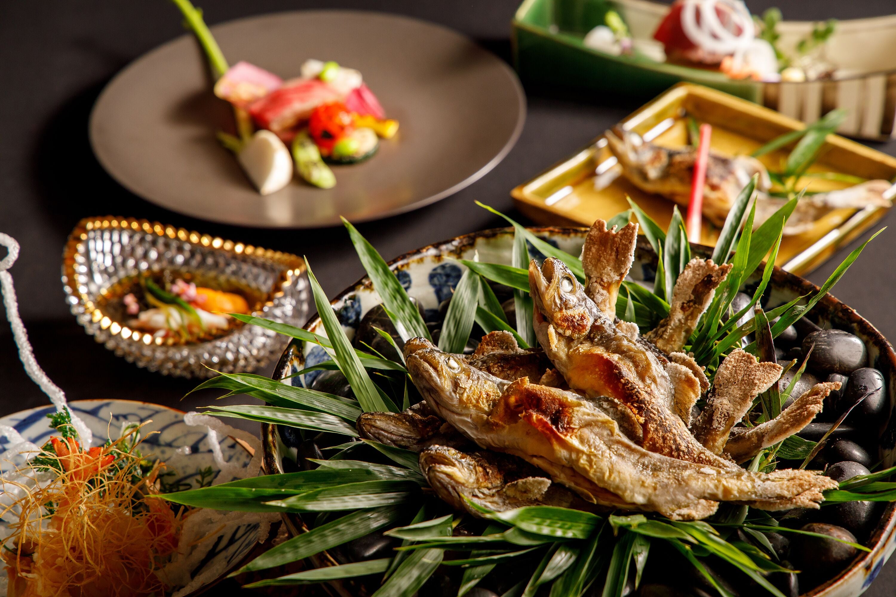 A variety of dishes including fried fish, vegetables, and a plate with watermelon and other items.