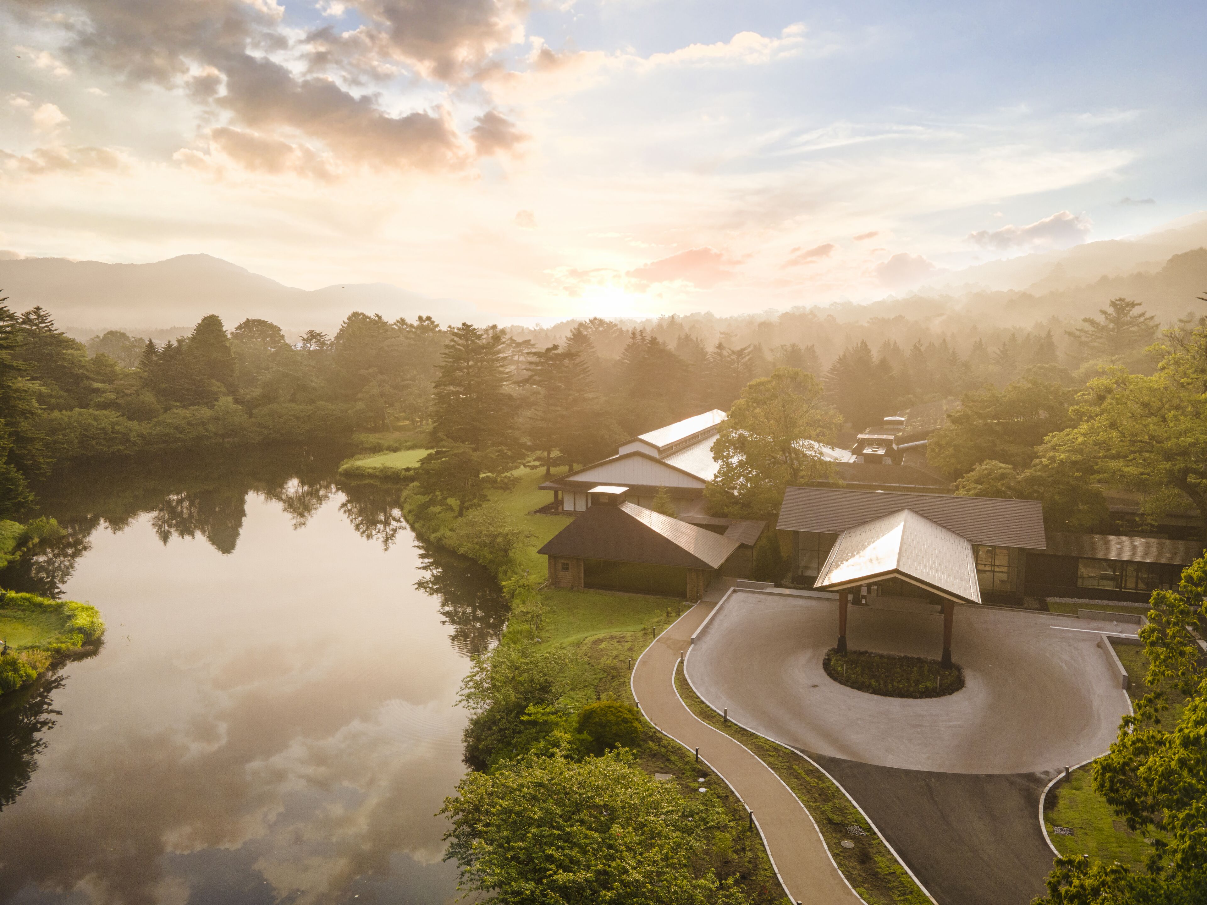 A serene lakeside property with a curved driveway, reflecting the surrounding greenery and buildings.