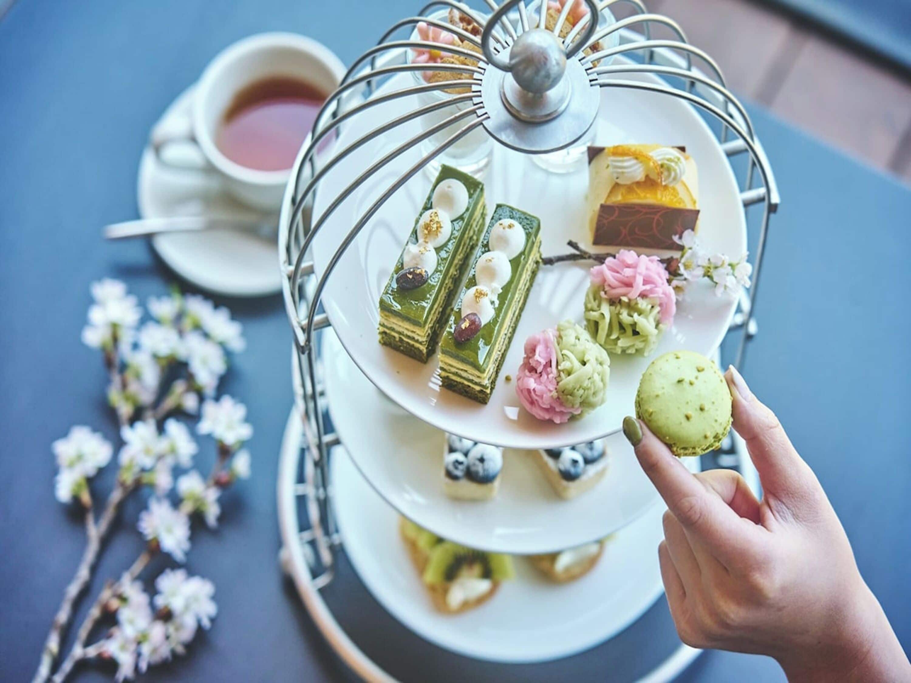 Un expositor escalonado para postres con varios pasteles y una taza de té sobre una mesa.