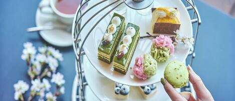 Un expositor escalonado para postres con varios pasteles y una taza de té sobre una mesa.