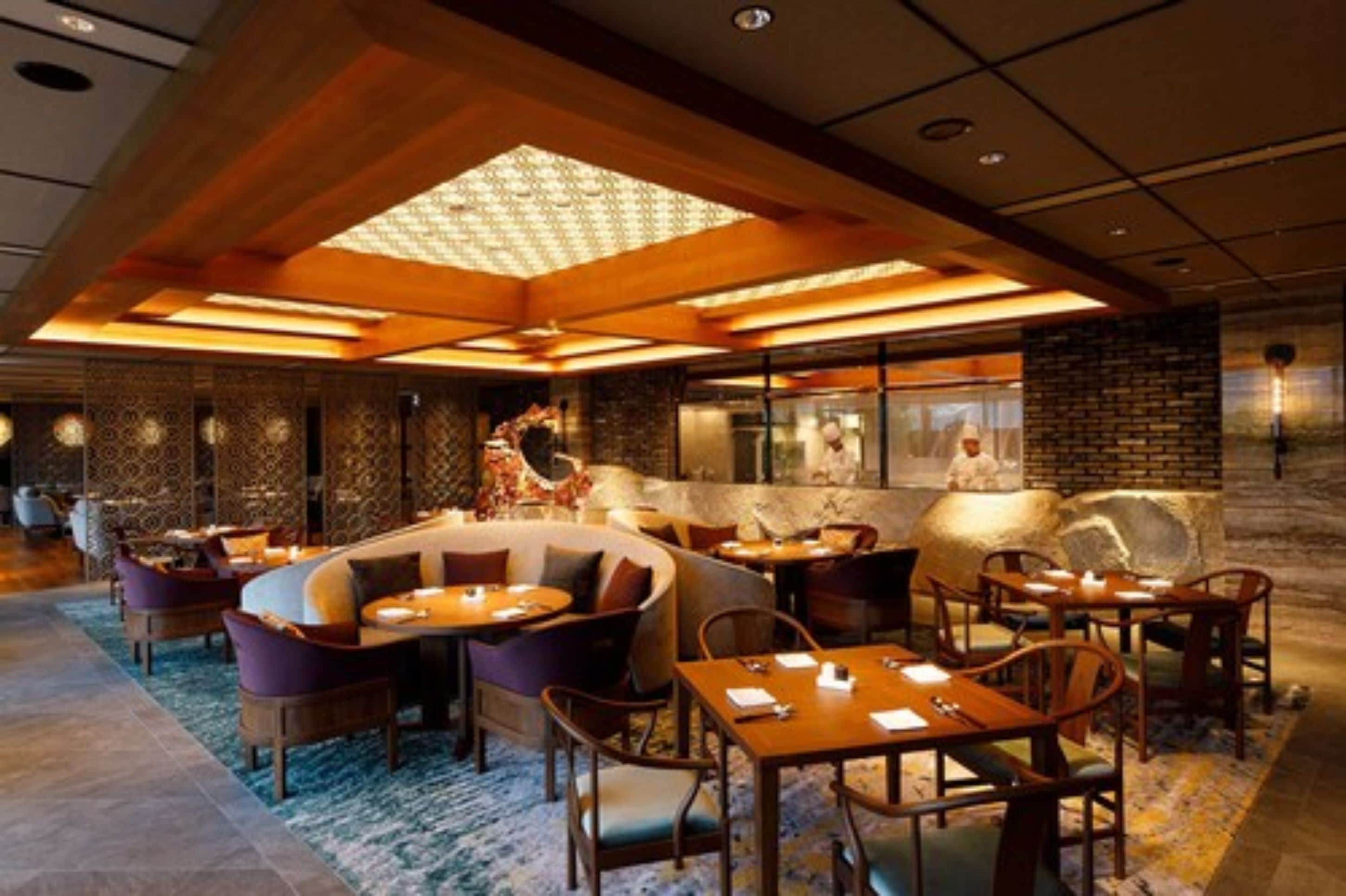 Un restaurante moderno con una zona de asientos central, mesas individuales y una barra.