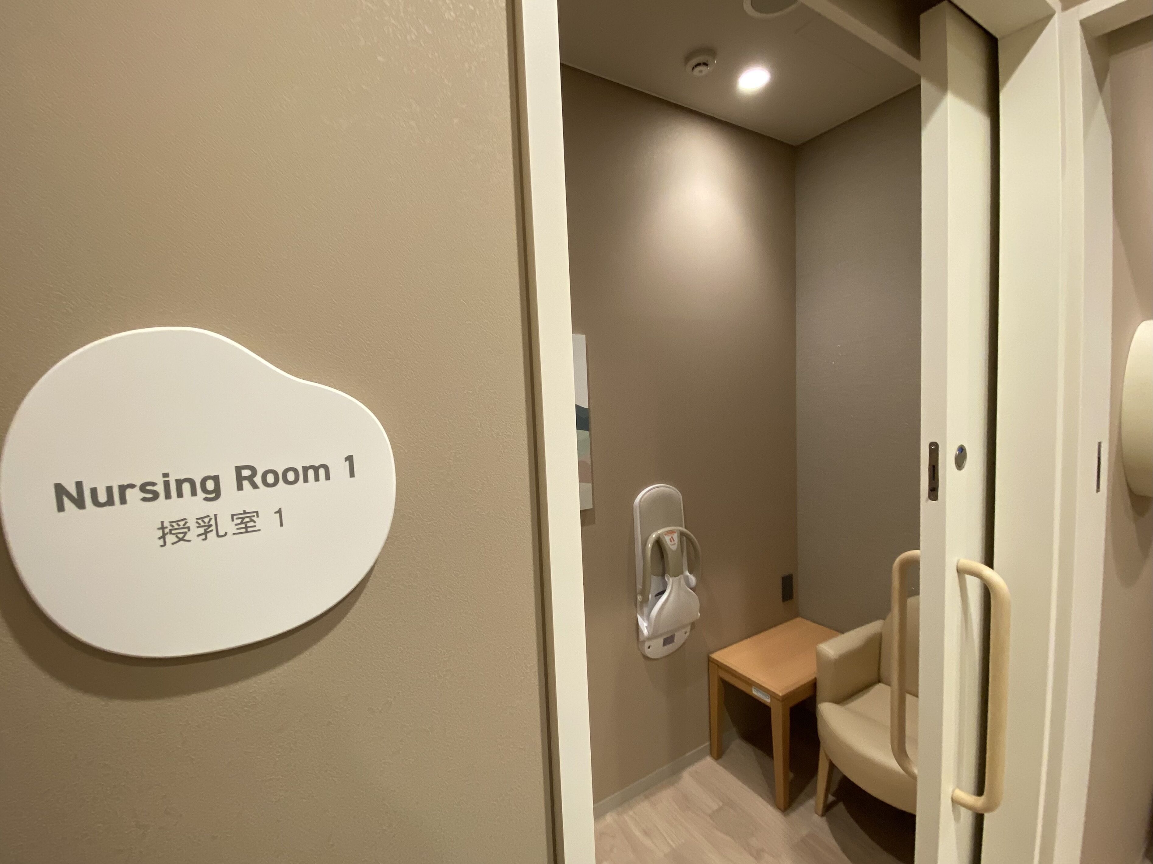 A nursing room with a sign, a small table, a chair, and a handrail.