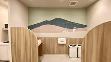 A children's bathroom with a mural of a landscape, wooden partitions, and a trash bin.