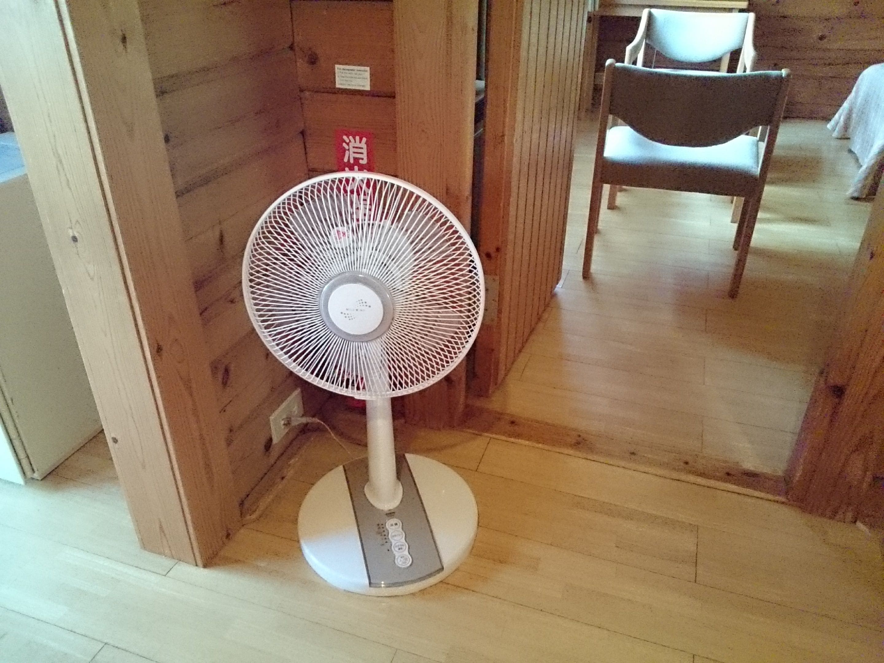 A standing fan in a room with wooden walls and a wooden floor.