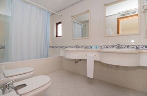 A bathroom with a bathtub, two sinks, a toilet, and a mirror. - Hotel Apartamento do Golfe (Loulé)