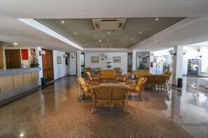 A spacious lobby with a polished floor, a reception desk, wicker furniture, and framed artwork on the walls. - Hotel Apartamento do Golfe (Loulé)