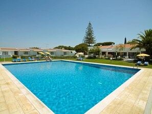 A rectangular swimming pool with clear blue water, surrounded by a tiled deck. There are lounge chairs and umbrellas along the poolside. - Hotel Apartamento do Golfe (Loulé)