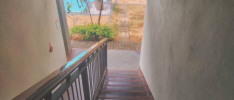 A staircase with a metal railing leading to an outdoor area with a pool and palm trees.