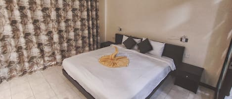 Una habitación de hotel con una cama, una mesita de noche, una lámpara de pared y una cortina con estampado de hojas.