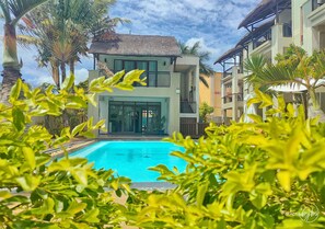 A hotel with a swimming pool, surrounded by lush greenery and palm trees. - Grand Bay Suites (Grand-Baie)