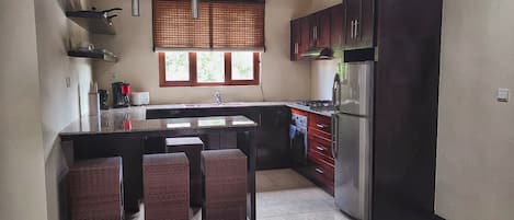 A kitchen with a central island, dark cabinets, a stainless steel refrigerator, and a window with blinds.