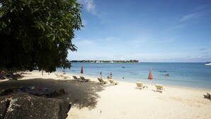 A beach with sun loungers and umbrellas, a clear sky, and calm water. - Grand Bay Suites (Grand-Baie)