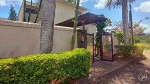 A gated entrance with a palm tree and a building with a flat roof. - Grand Bay Suites (Grand-Baie)