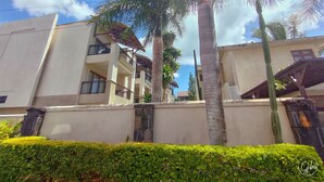 A multi-story building with balconies, palm trees, and a stone wall. - Grand Bay Suites (Grand-Baie)