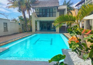 A swimming pool with a clear blue water, surrounded by a wooden deck and a house with a balcony. - Grand Bay Suites (Grand-Baie)