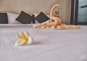 Una cama con una colcha blanca, un cojín decorativo con forma de cisne y una flor blanca.