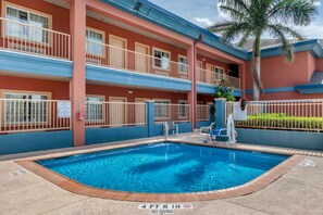 A swimming pool with a no diving sign, surrounded by a multi-story building with balconies and a palm tree.
