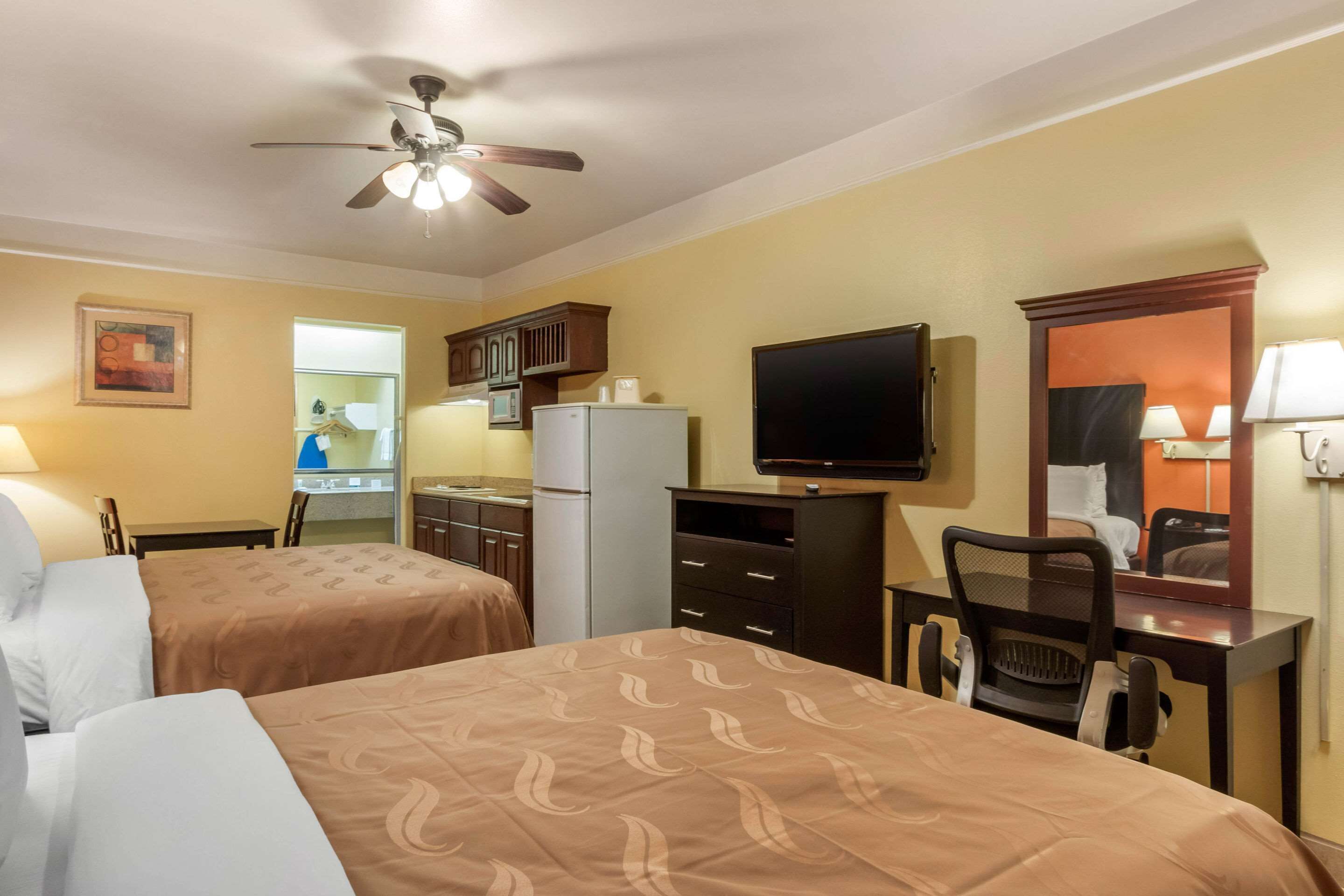 A hotel room with two beds, a desk, a chair, a television, and a ceiling fan.