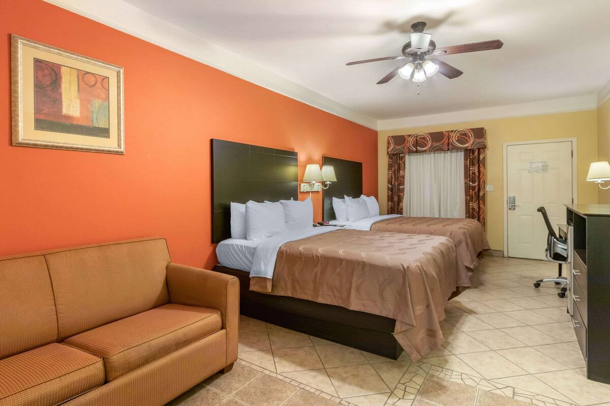 A hotel room with a bed, a sofa, a ceiling fan, and a painting on the wall.
