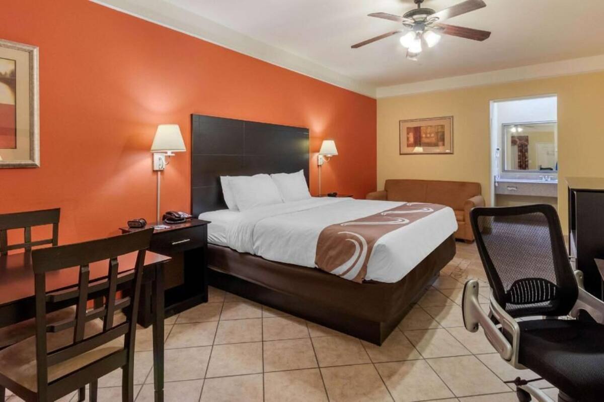 A hotel room with a bed, desk, chair, and a ceiling fan.