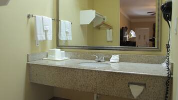 A bathroom with a granite countertop, a sink, a mirror, and a hairdryer mounted on the wall.