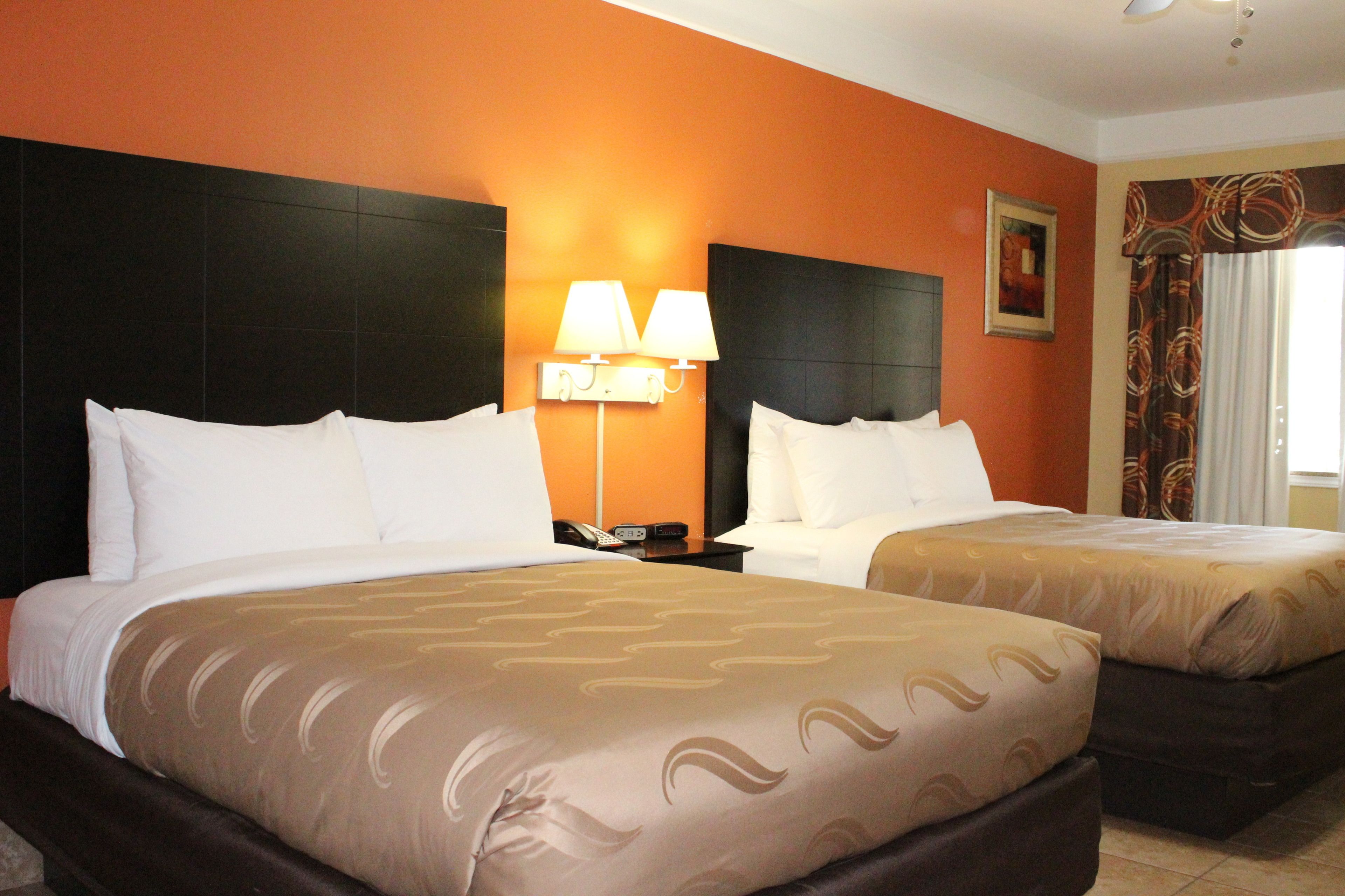 A hotel room with two beds, a nightstand with a lamp, and a painting on the wall.