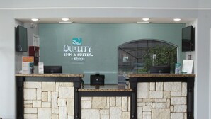 A reception desk with a stone facade, a glass partition, and a sign for Quality Inn & Suites. - Quality Inn & Suites at The Outlets Mercedes/Weslaco (Mercedes)
