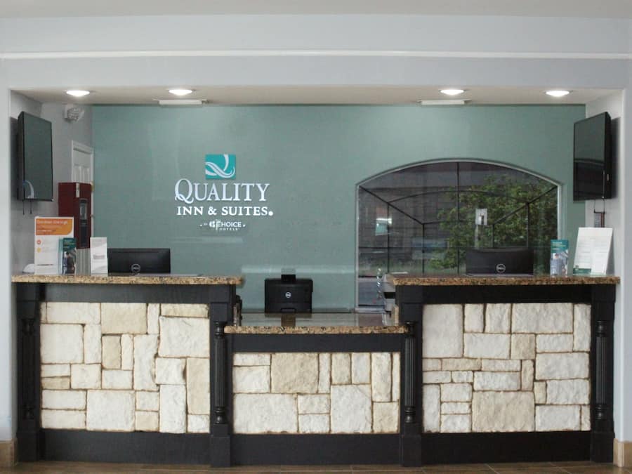 Ein Empfangsschalter mit Steinverkleidung, einer Glastrennwand und einem Schild für Quality Inn & Suites.