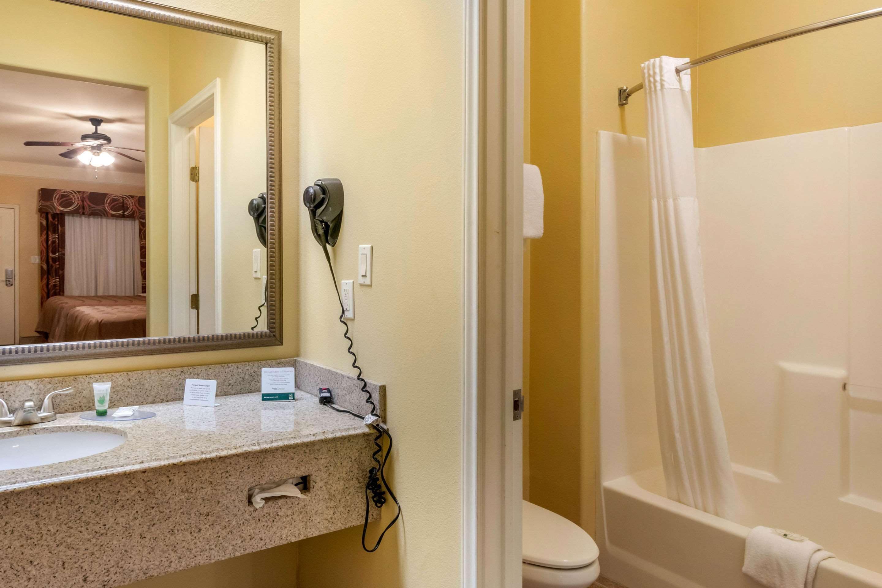 Un baño con lavamanos, espejo, secador de pelo y una ducha con cortina.