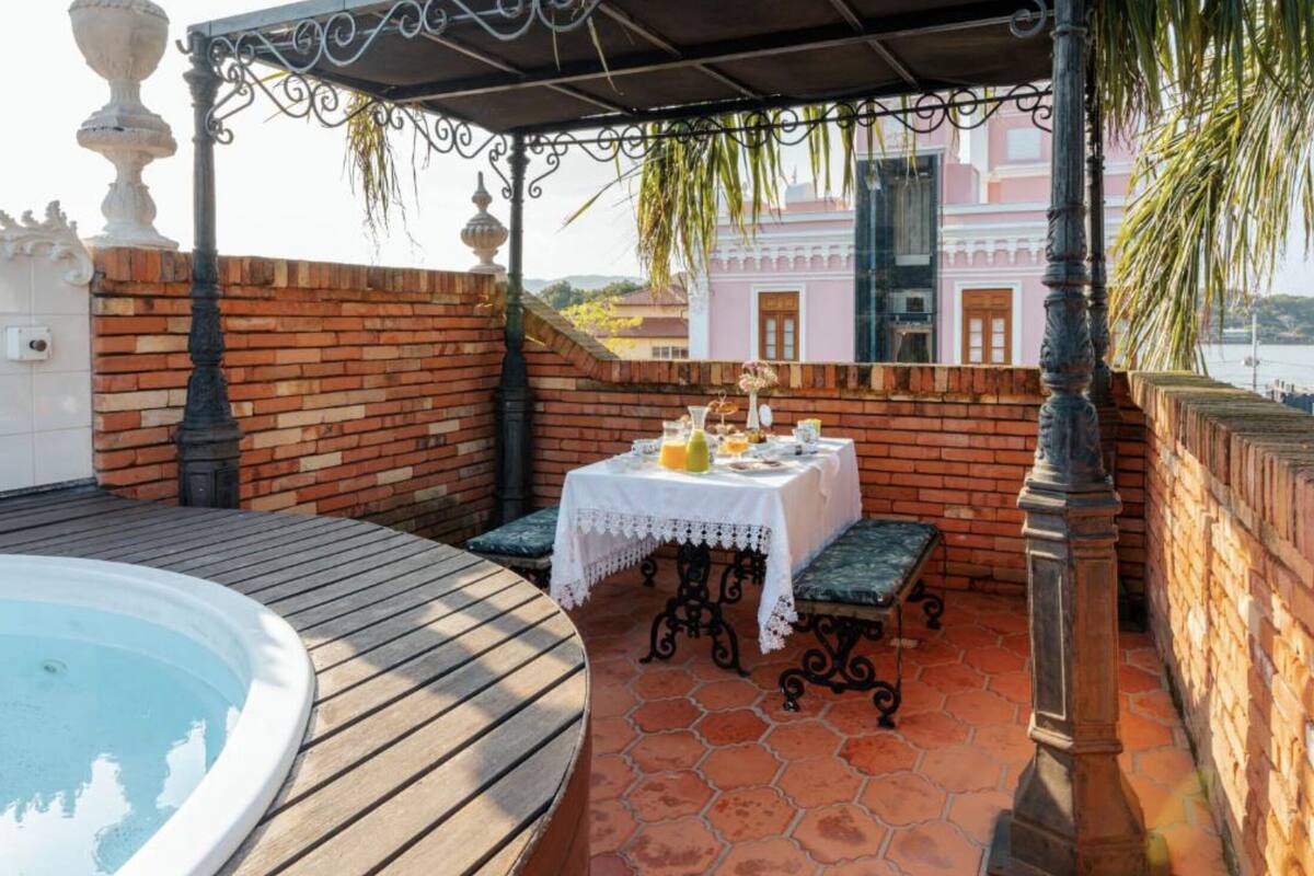 Een terras op het dak met een jacuzzi, een tafel met drankjes en uitzicht op een roze gebouw.