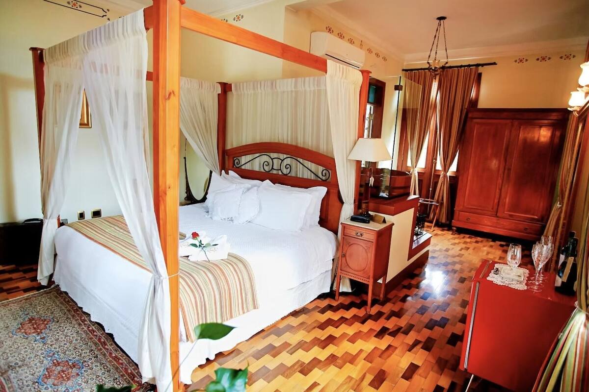 Een hemelbed, een nachtkastje met een lamp, een rode nachtkastje en een houten garderobe.