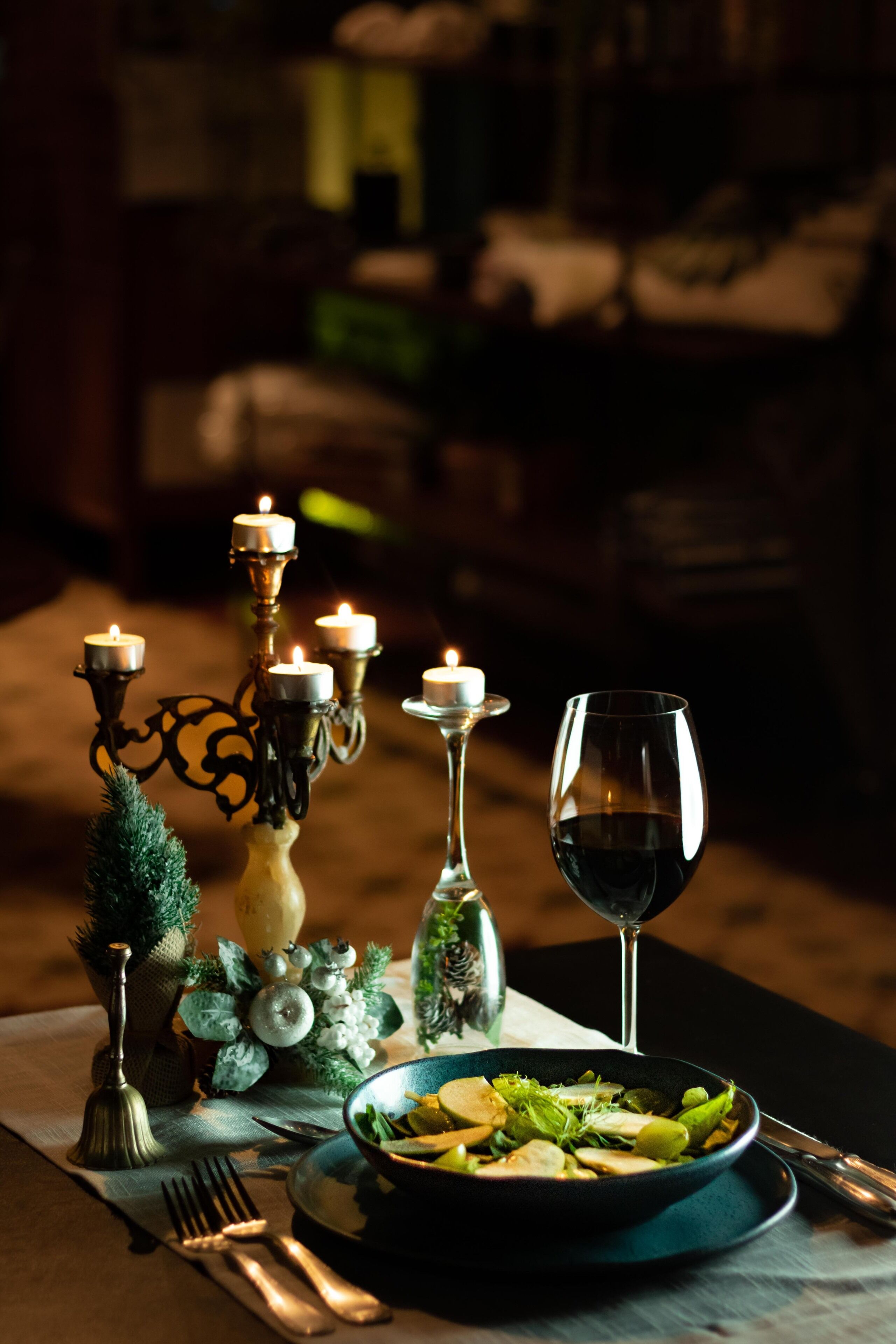 Un tavolo apparecchiato con un'insalata in una ciotola, un bicchiere da vino e un candelabro con candele accese.