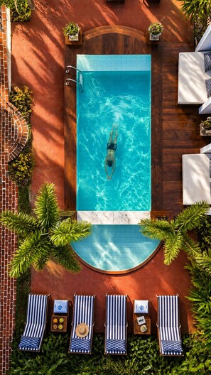 An outdoor swimming pool with a person swimming, surrounded by lounge chairs and potted plants.