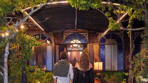 A couple walking on a red carpet towards a building with a covered entrance and decorative lighting.