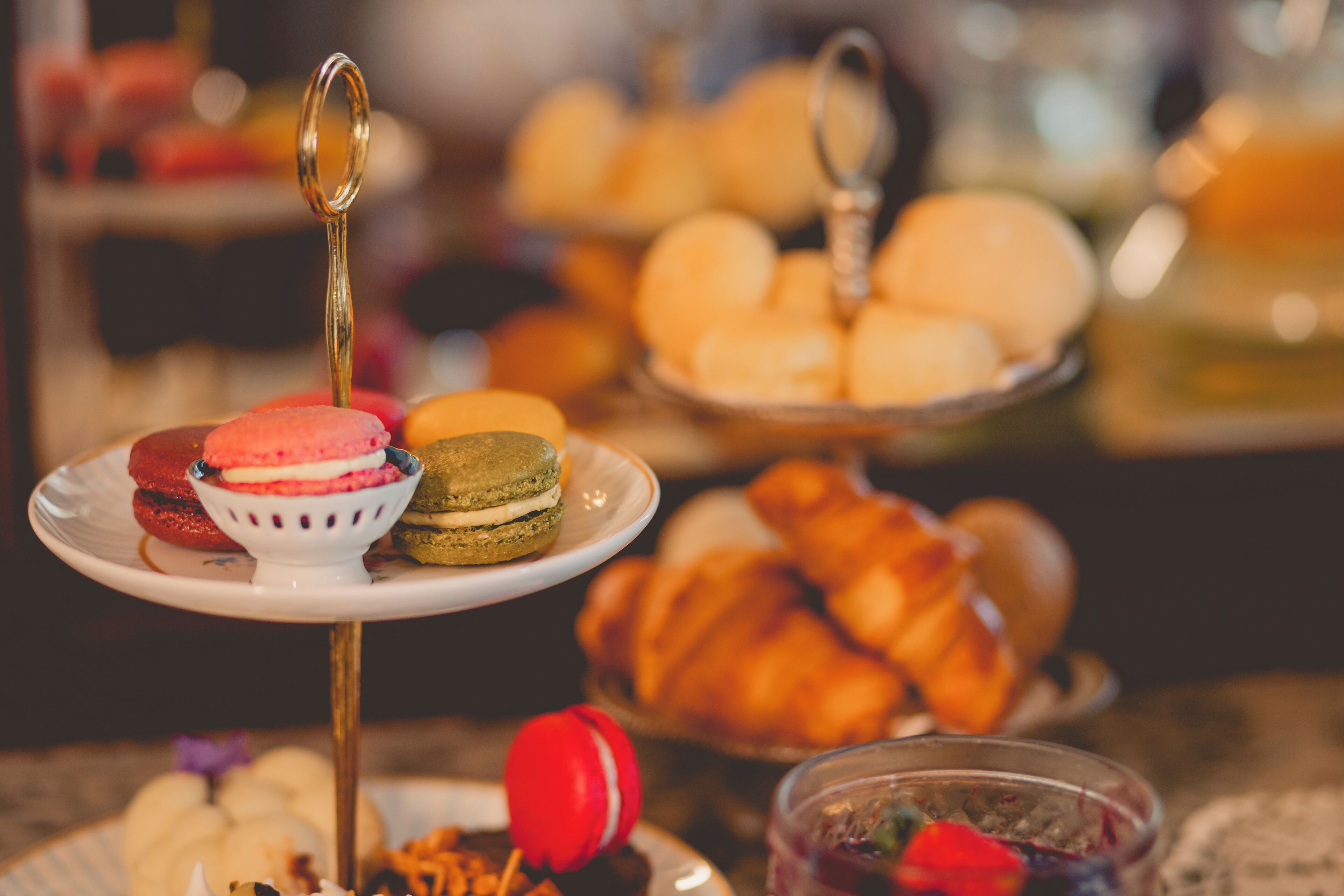 A tiered dessert stand with macarons, a croissant, and a bowl of fruit.