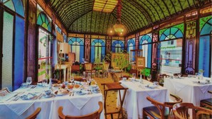 A dining area with tables set for meals, a high arched ceiling, and large windows with stained glass.