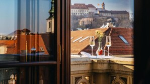 A table with two glasses of wine and a vase of flowers, overlooking a historic building with a clock tower. - Grand Palace Brno - Small Luxury Hotels of the World (Brno)