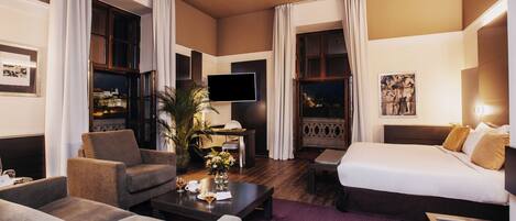 A hotel room with a sofa, a bed, a TV, a dining table, and a window with curtains.