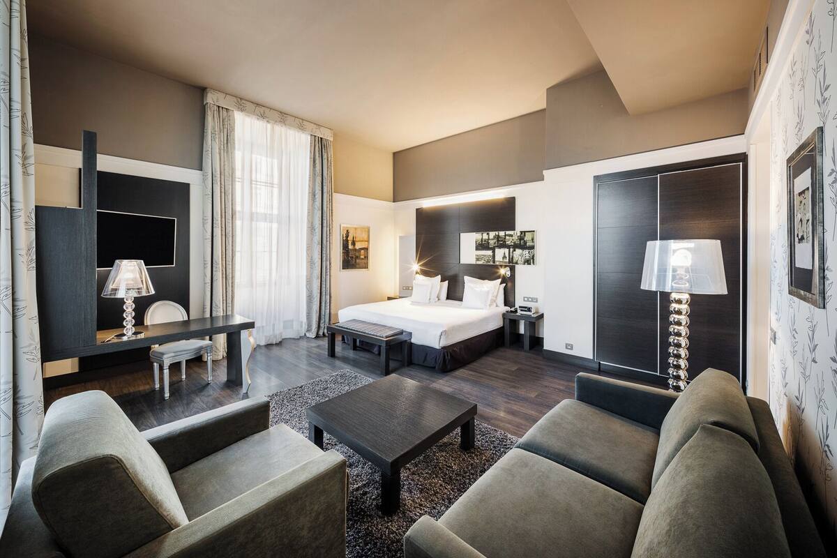 A hotel room with a bed, a desk, a chair, a sofa, and a lamp.