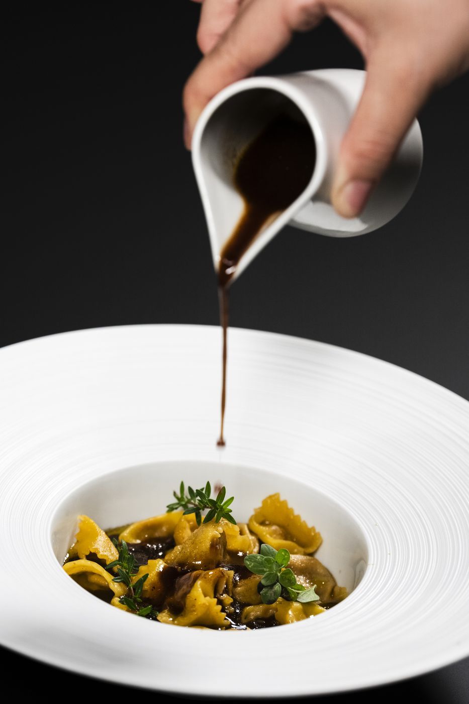 A hand pouring sauce over a dish of pasta.