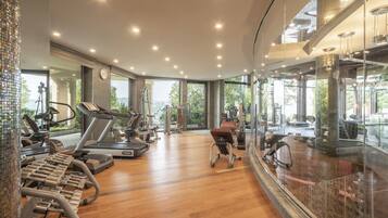 A modern gym with various exercise equipment, large windows, and a wooden floor.
