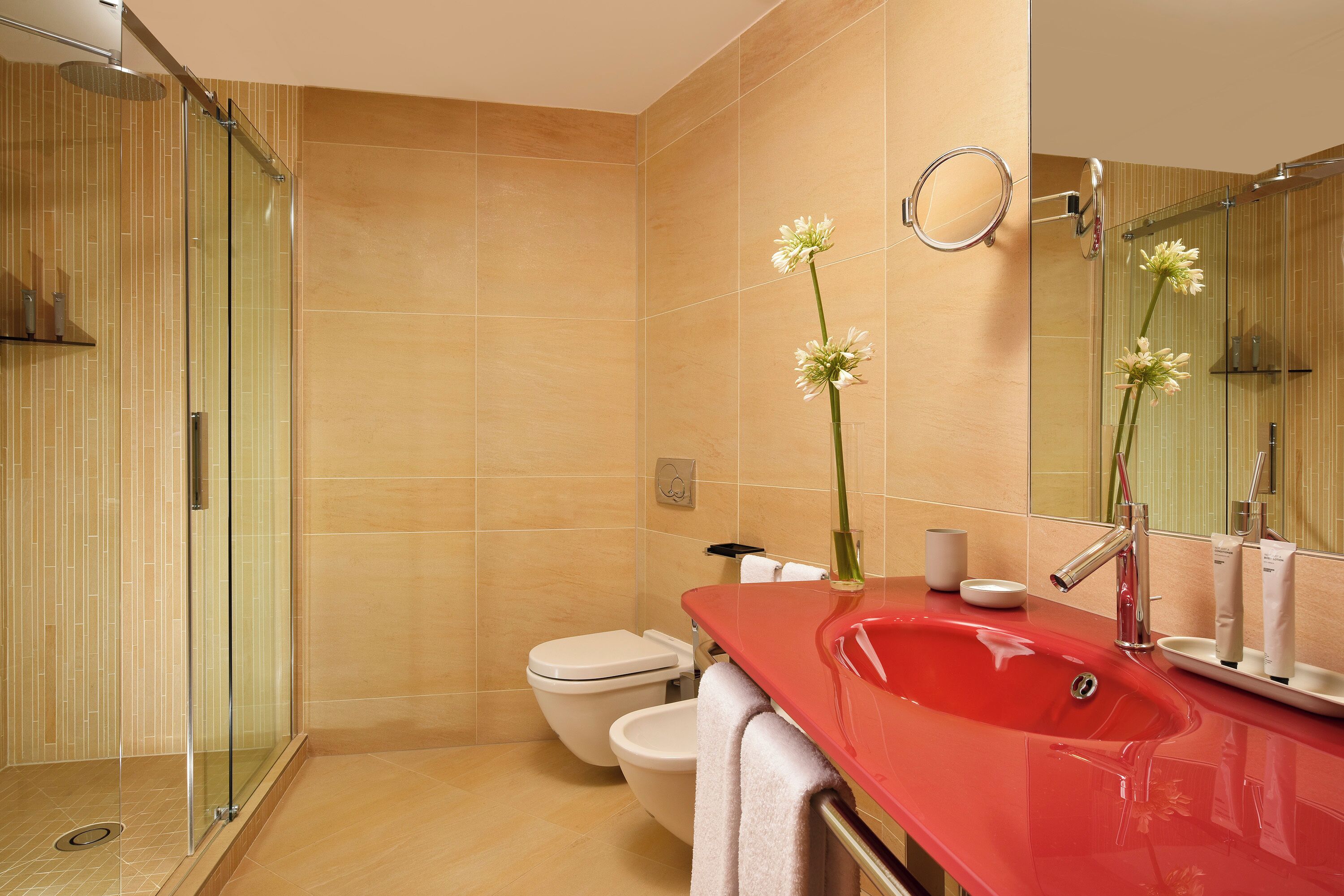 A modern bathroom with a glass-enclosed shower, a red sink, and a toilet.