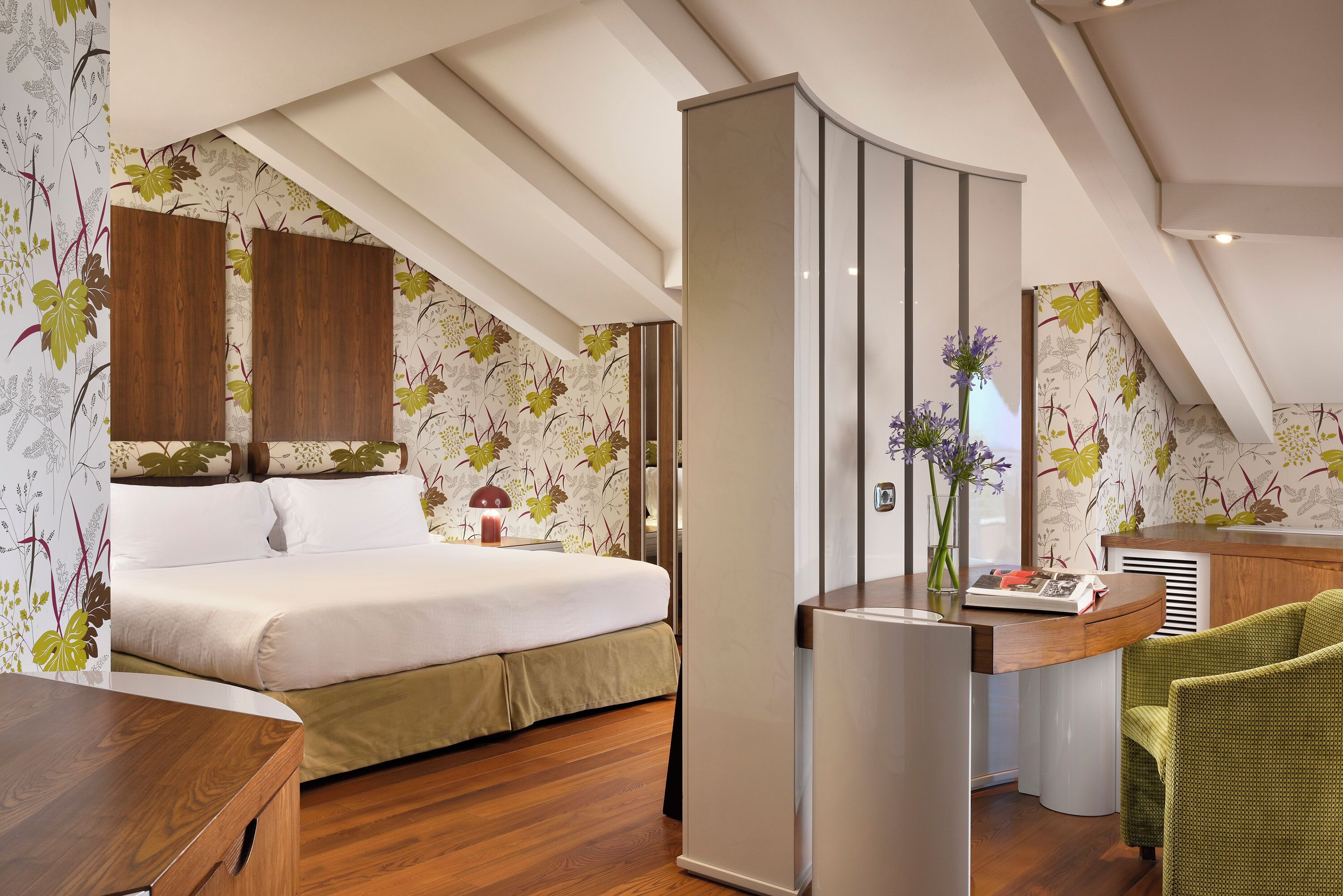 A bedroom with a bed, a desk, a chair, and a kitchenette.