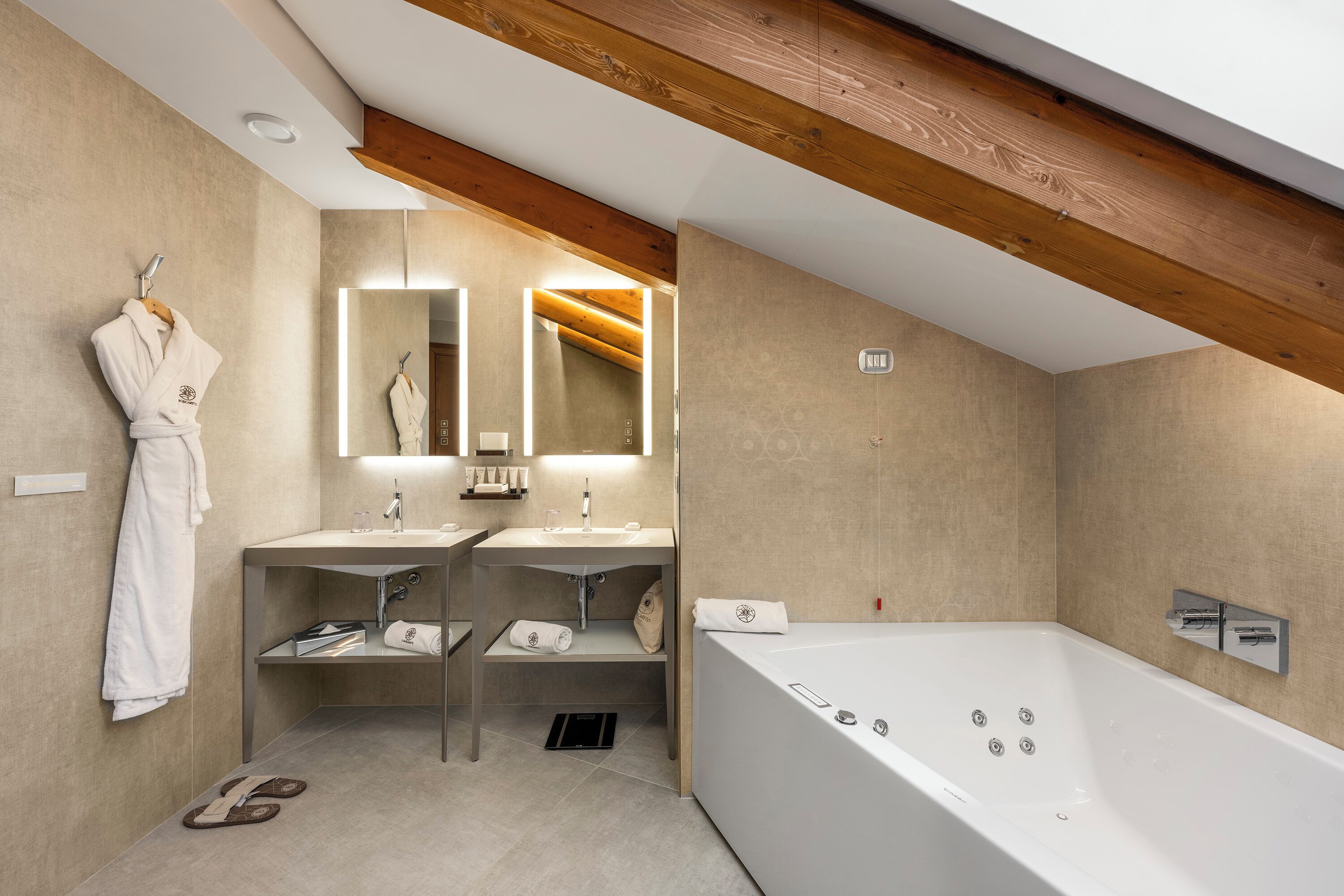 Ein modernes Badezimmer mit einer großen Badewanne, zwei Waschbecken, einem Spiegel und einem Bademantel, der an einem Wäscheständer hängt.