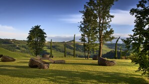 A grassy field with large, round seating areas and tall trees. - Il Boscareto Resort & Spa (Serralunga d'Alba)