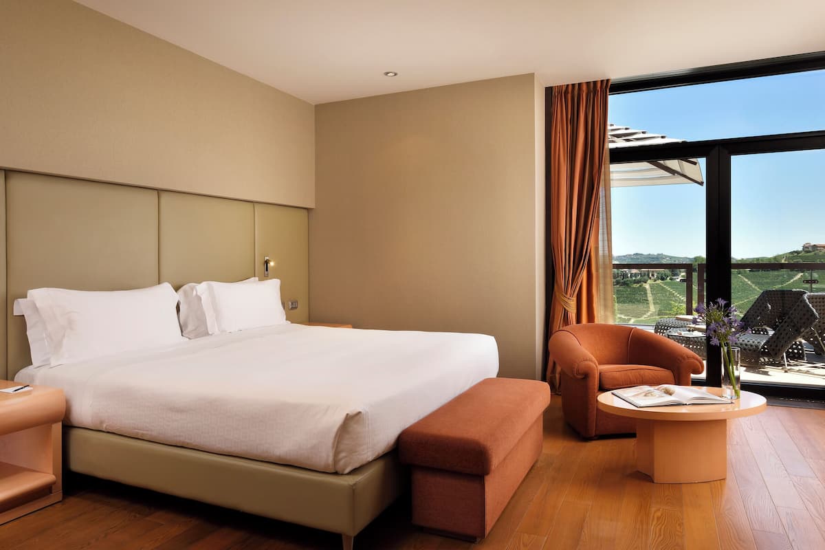 A hotel room with a large bed, a sofa, a small table, and a view of the outdoors.