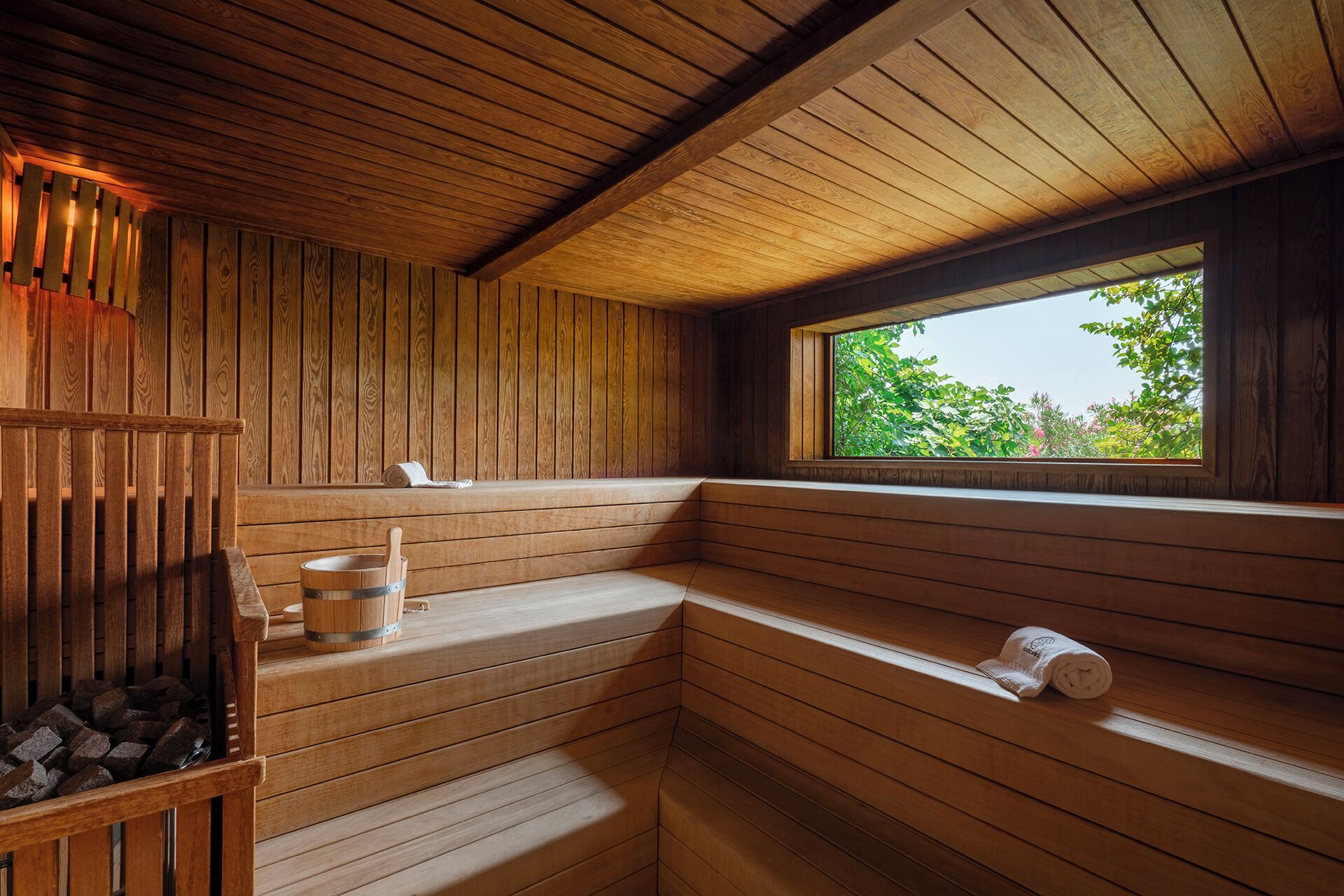 A wooden sauna with benches, a bucket, and a towel.